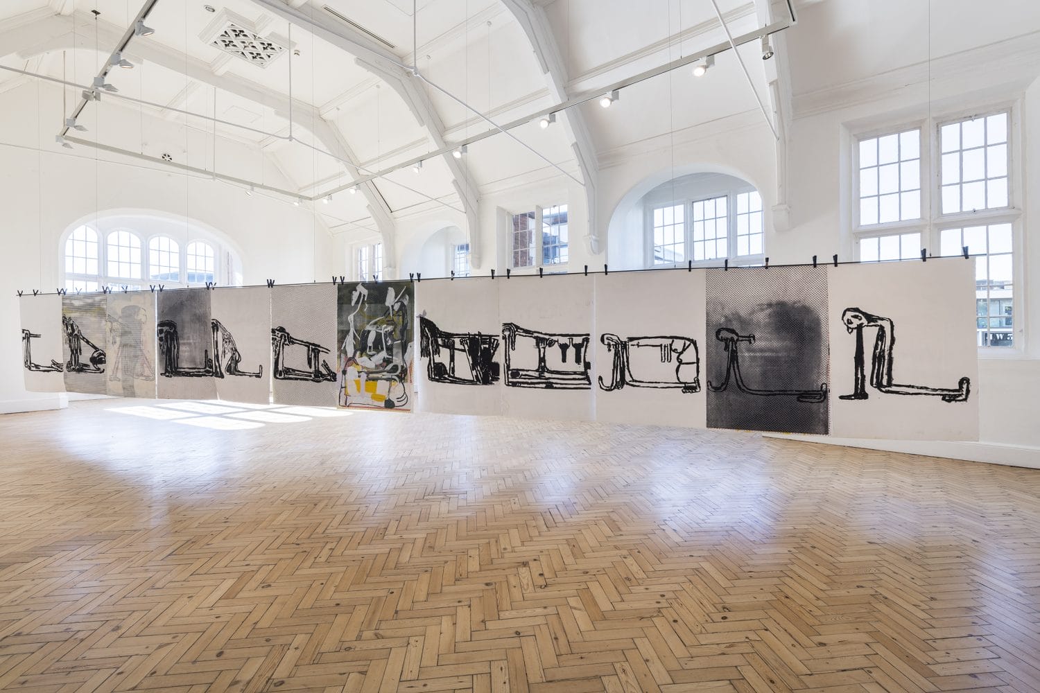 Art installation in a bright gallery with large abstract paintings on paper, wood floor, and high arched ceilings.