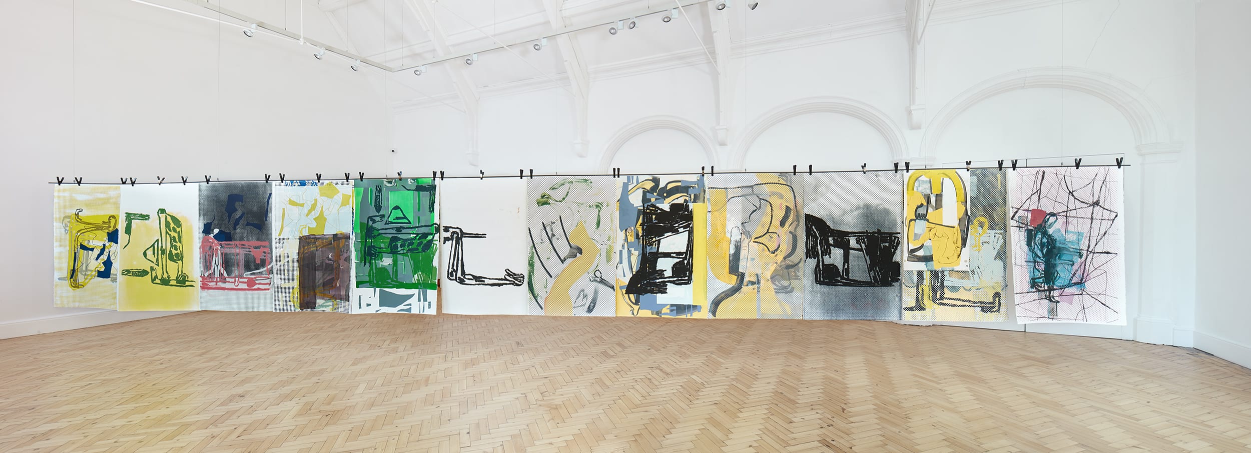 Art installation featuring a series of abstract paintings with various colors displayed in a spacious gallery setting.