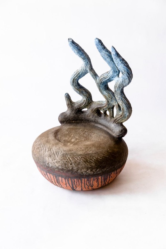 Sculptural ceramic piece with organic, wave-like blue forms rising from a textured, round brown base.