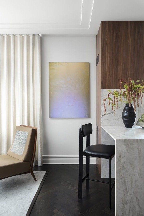 Modern living room with abstract art on white wall, cozy chair, marble bar, and vase of greenery on countertop