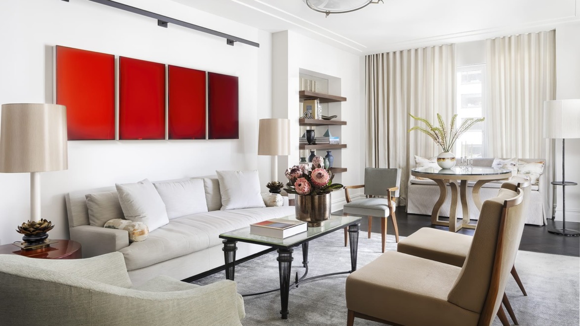 Modern living room with white sofa, red art on wall, chairs, table, and bright windows with sheer curtains.