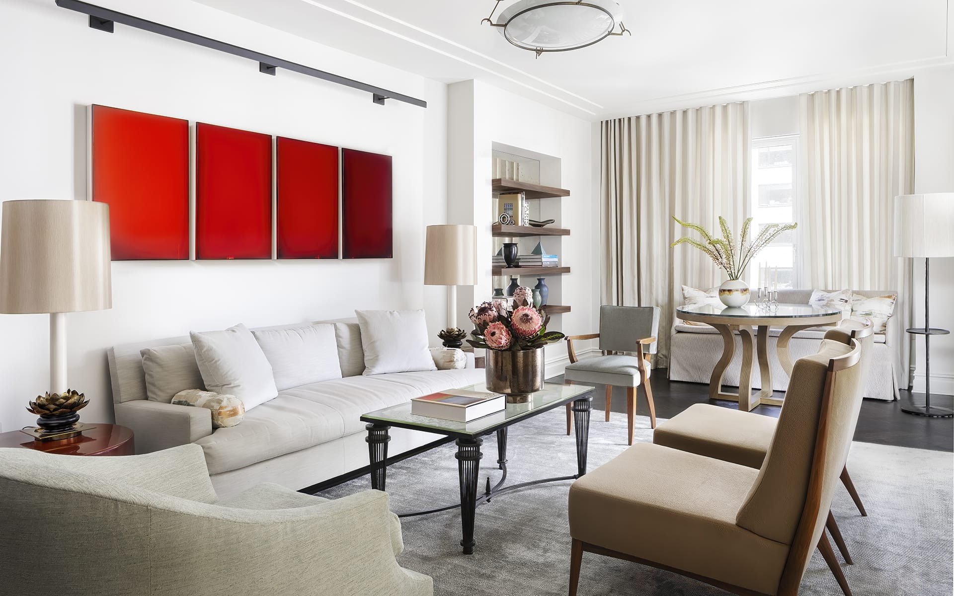 Modern living room with white sofa, red art on wall, chairs, table, and bright windows with sheer curtains.