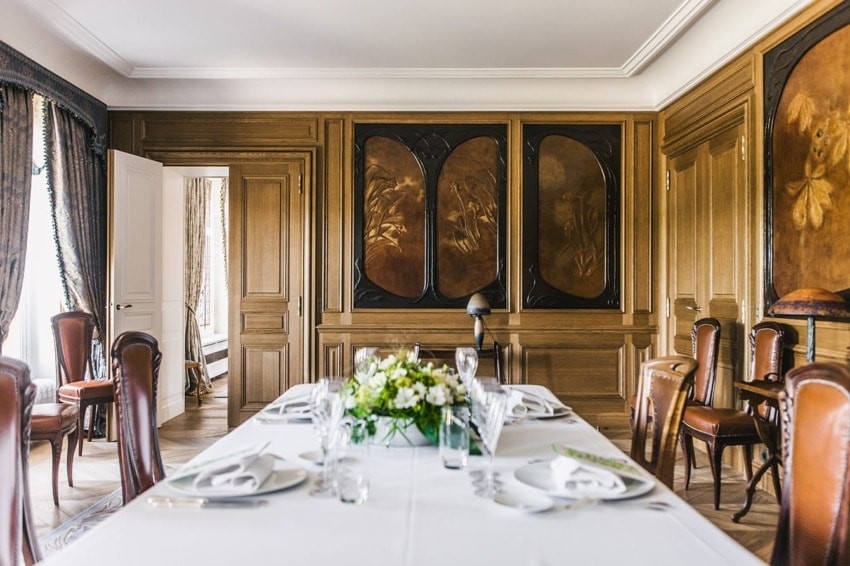 Elegant dining room with a white tablecloth, set for a formal meal, surrounded by wooden chairs and ornate wall panels.