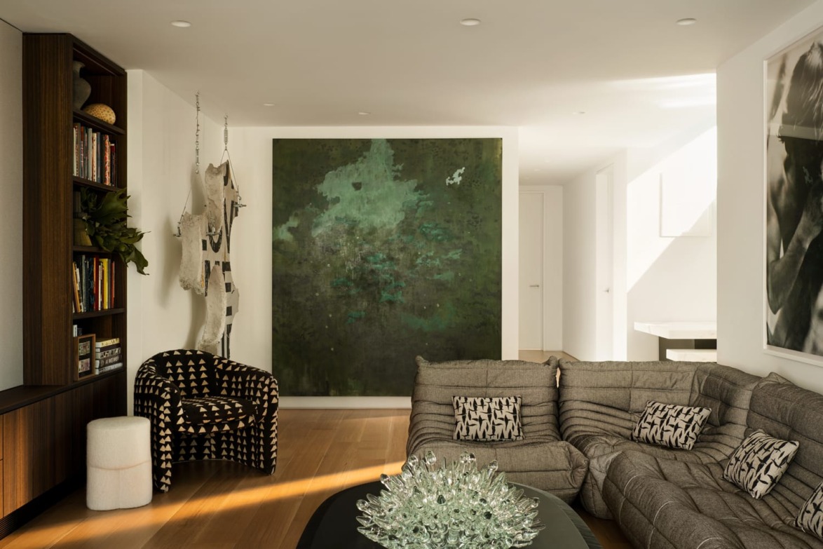 Stylish living room with large green abstract painting, gray sectional sofa, patterned chair, and bookshelf.