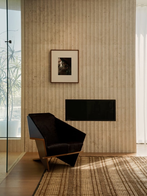 Modern living room with a black chair, textured wall, framed artwork, and large window with sunlight streaming in.
