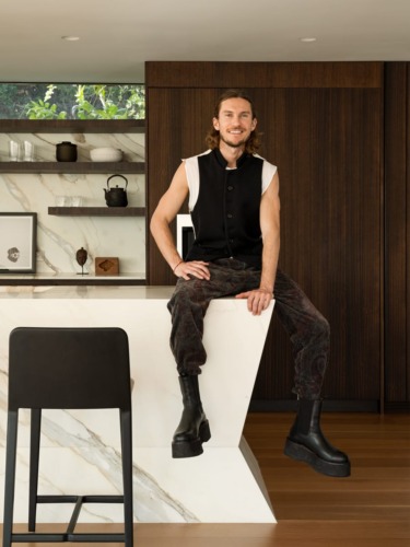 Person sitting on a modern kitchen counter wearing stylish black boots and patterned pants, with a wooden background.