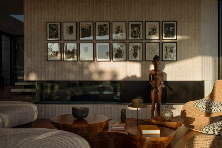 Modern living room with wall art, sculptures, and wooden tables with decorative items, featuring warm natural lighting.