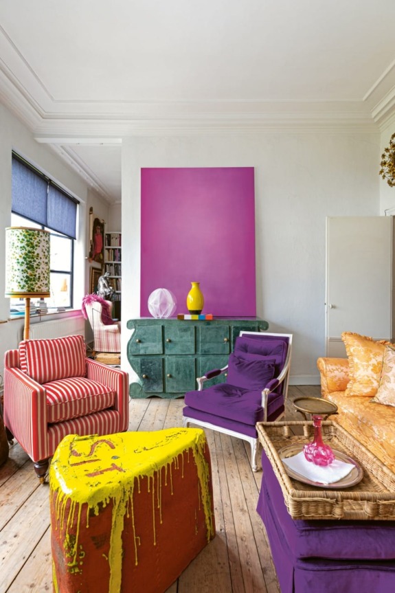 Colorful eclectic living room with striped and purple furniture, vibrant yellow vase, and large purple wall art.
