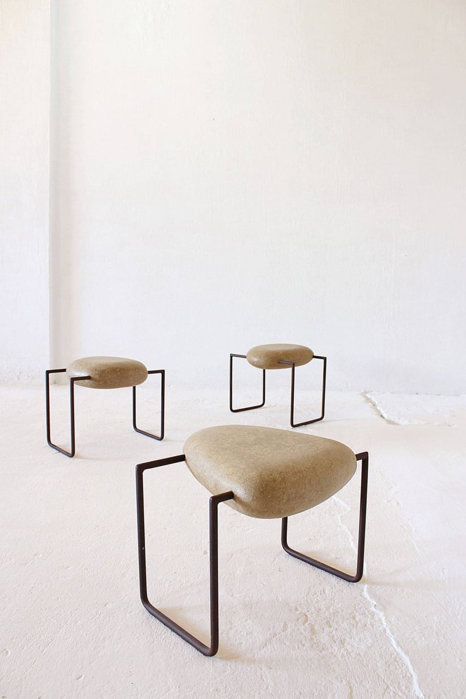 Three minimalist stools with beige cushioned seats and black metal legs on a light-colored floor in a bright room.