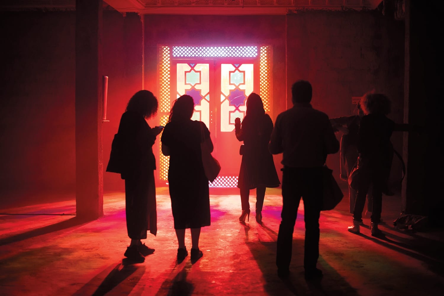 Silhouettes of five people standing in front of a vibrant, illuminated door in a dimly lit room with colorful light effects.
