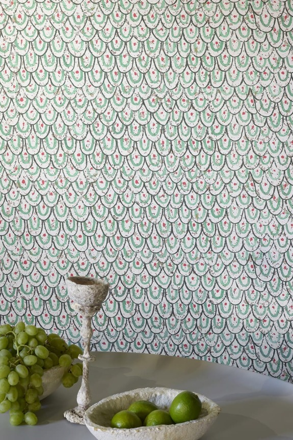 Decorative wall pattern with green and pink arches, lime-filled bowl on table, surrounded by grapes and a decorative chalice.