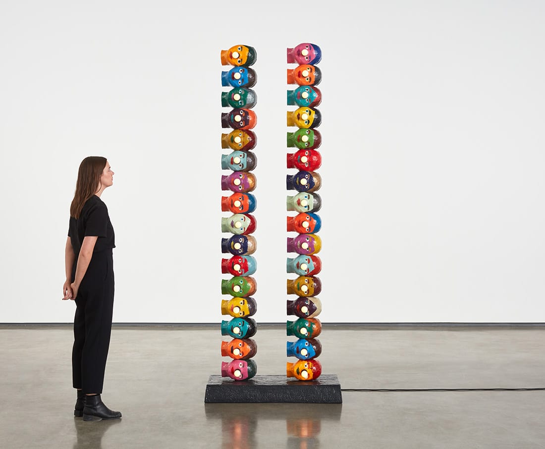 Woman admiring tall colorful totem-like sculpture in a gallery setting.