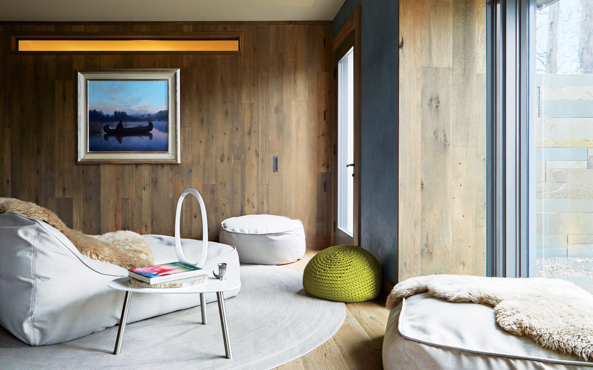 Modern living room with wooden walls, abstract art, cozy seating, and large window providing natural light.