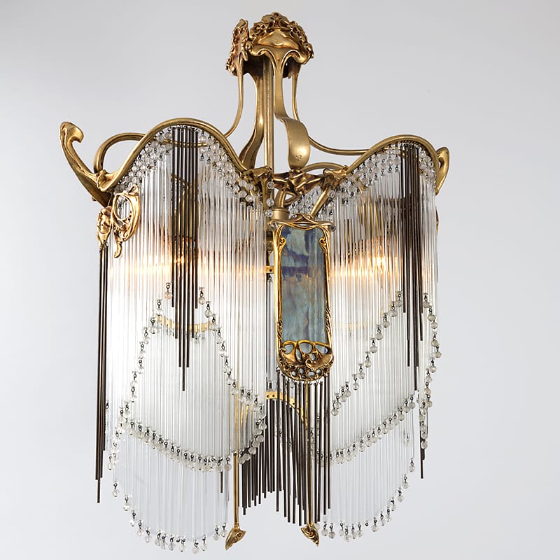 Art Nouveau chandelier with ornate bronze frame and crystal fringe, featuring intricate decorative elements and soft lighting.