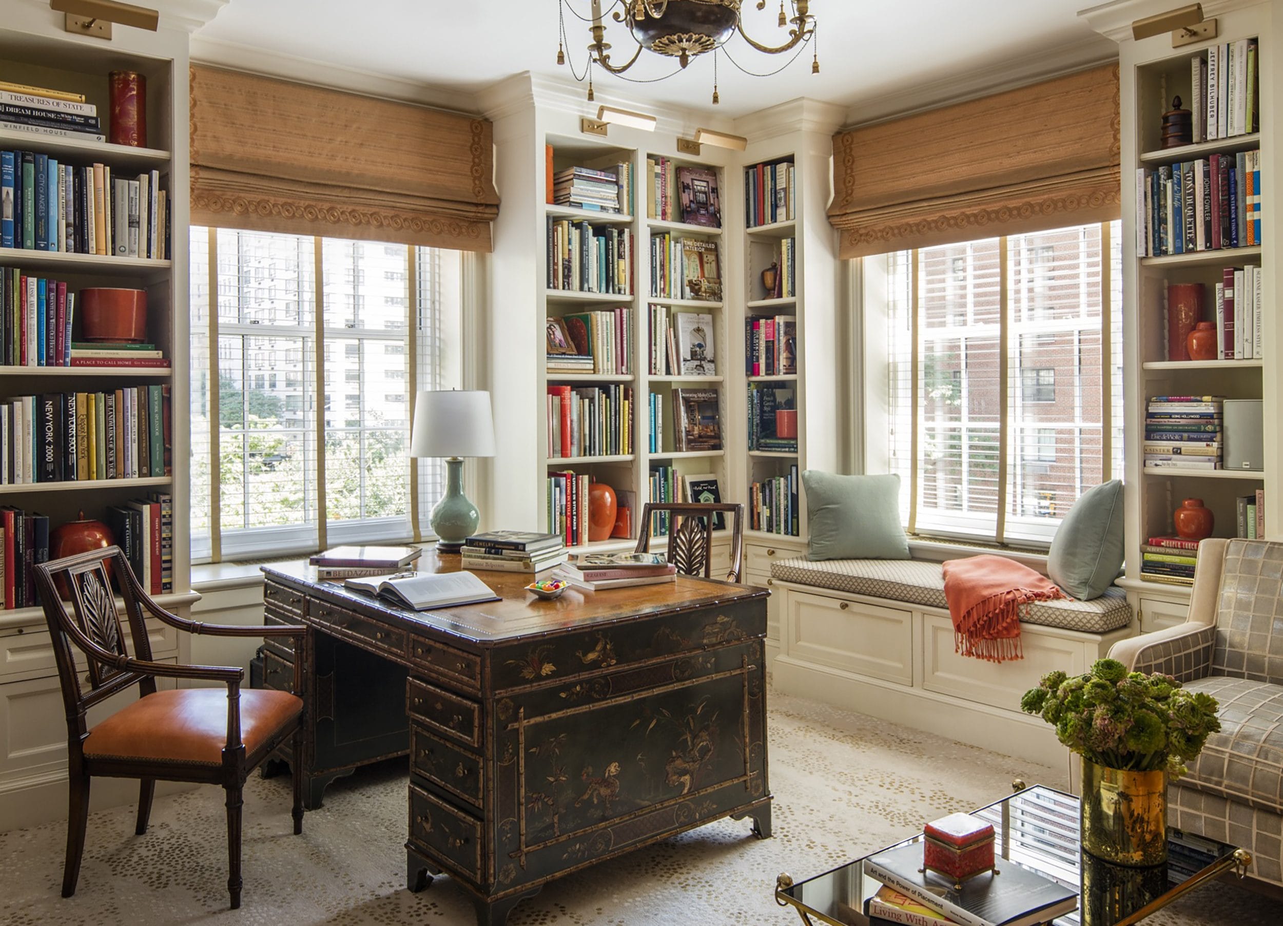 Elegant home office with a vintage desk, wooden chair, bookshelves, large windows, and cozy window seating with cushions.
