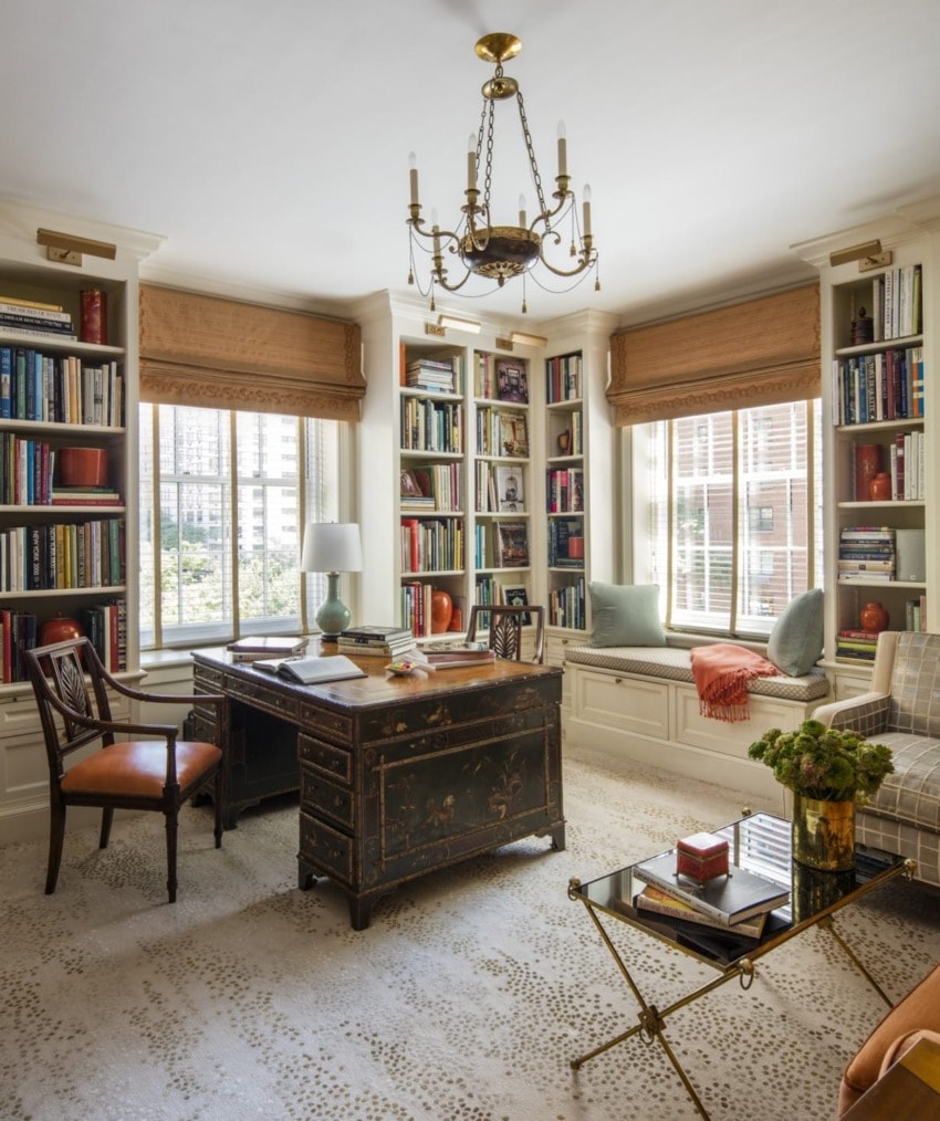 Elegant home office with a vintage desk, bookshelves, cozy seating, large windows, chandelier, and decorative accents.