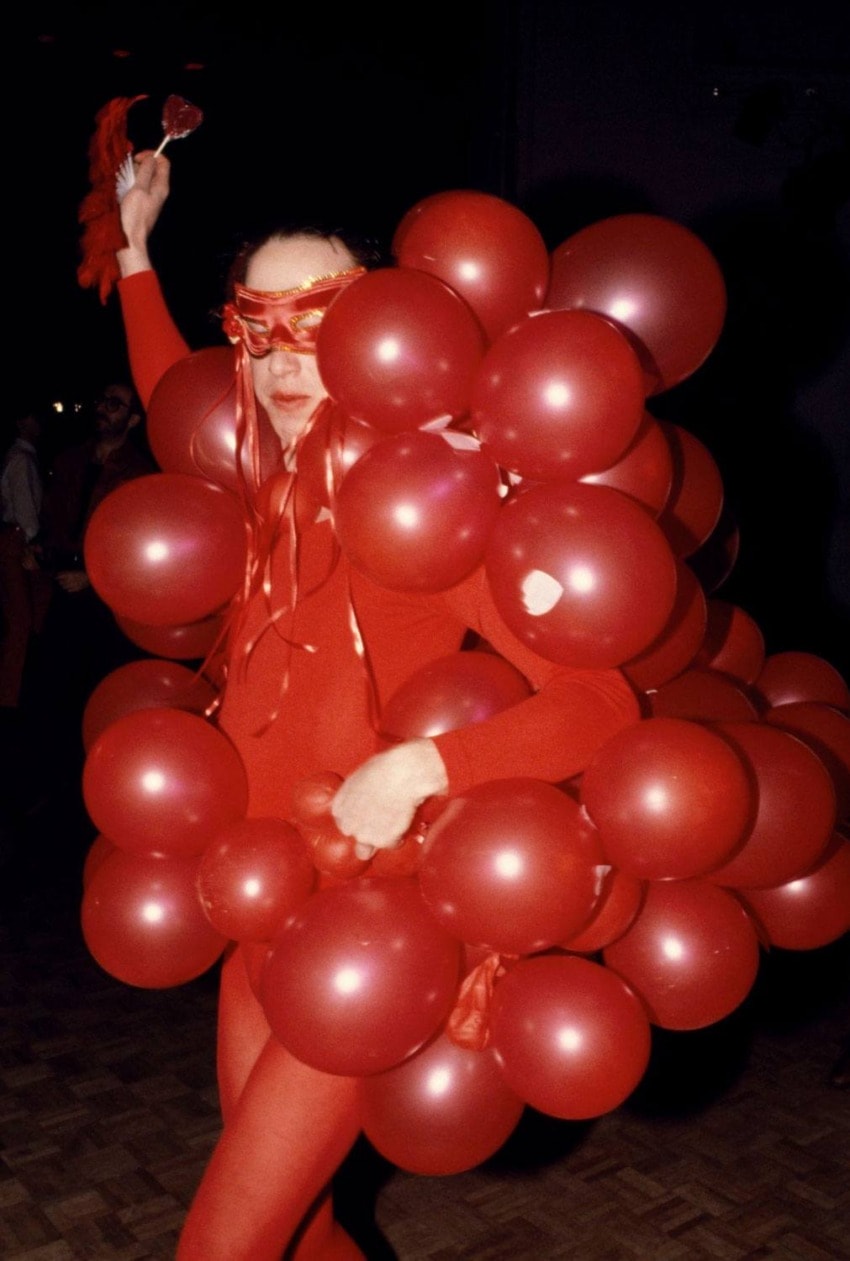 Person wearing a red costume covered in red balloons and a mask at a festive event.