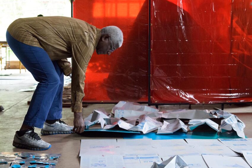 Person arranging art pieces on the floor in a studio with a red backdrop in the background.