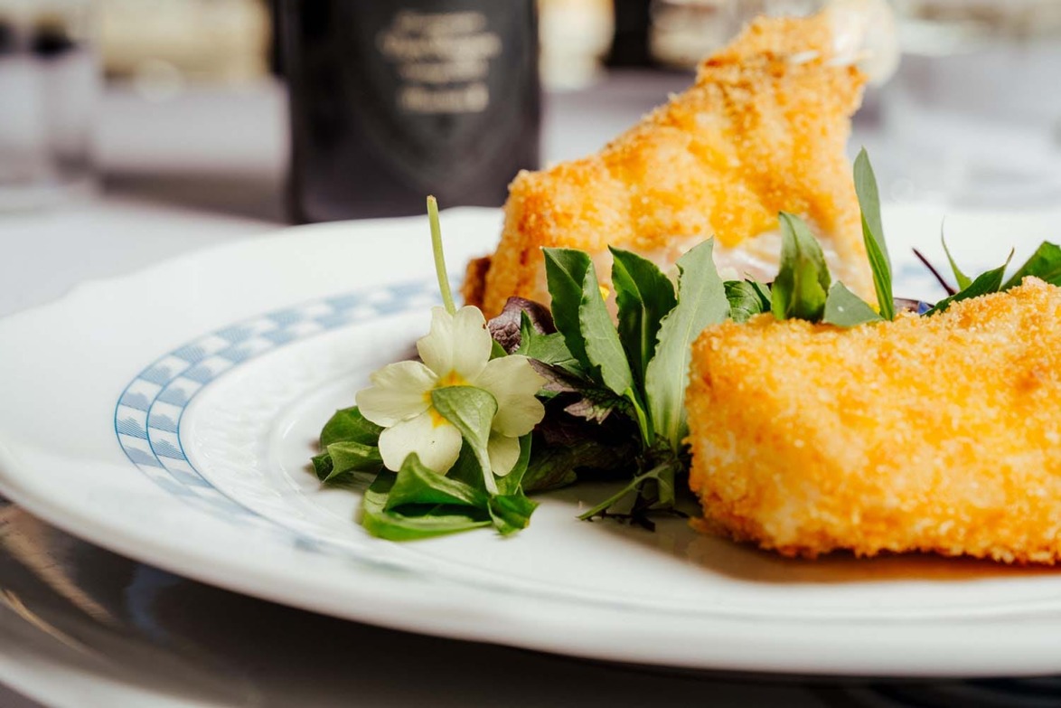Crispy breaded fish fillets served on a plate with fresh greens and a decorative flower garnish.