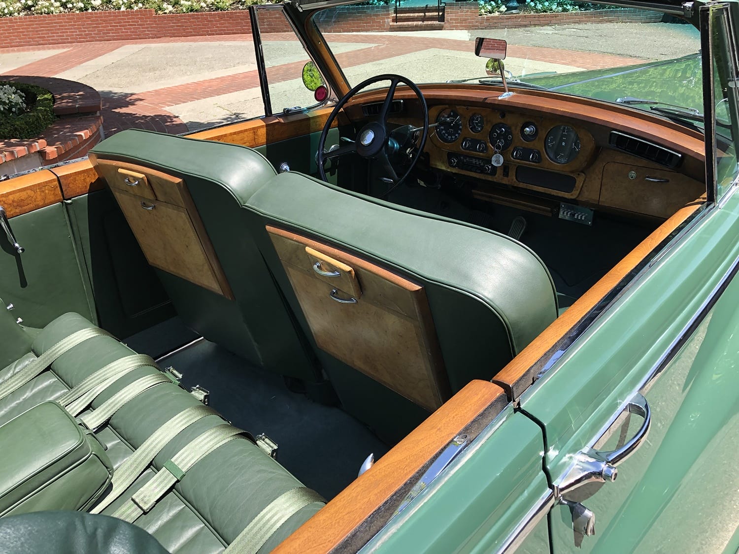 Interior of a vintage car with green leather seats and wooden dashboard detailing.