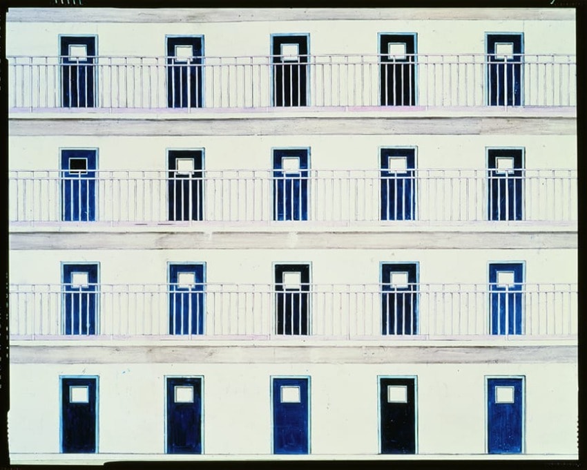 Building facade with multiple rows of identical blue doors and white windows, organized in a symmetrical pattern.
