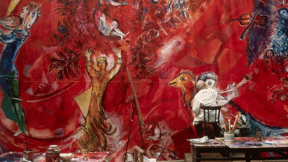 An artist painting a vibrant red mural with abstract figures and bold brush strokes in a studio setting.