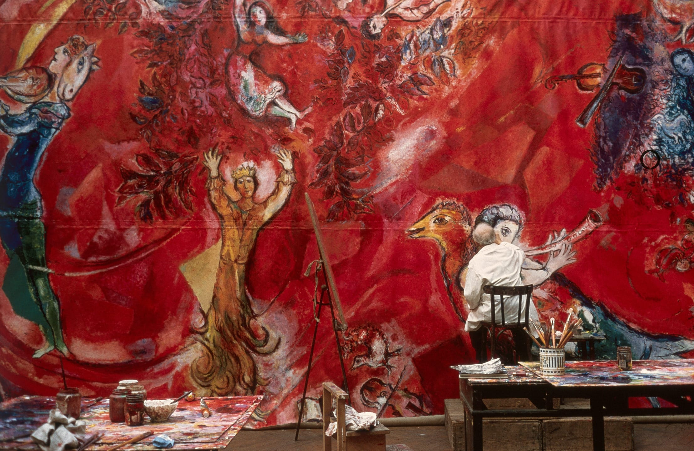 An artist painting a vibrant red mural with abstract figures and bold brush strokes in a studio setting.