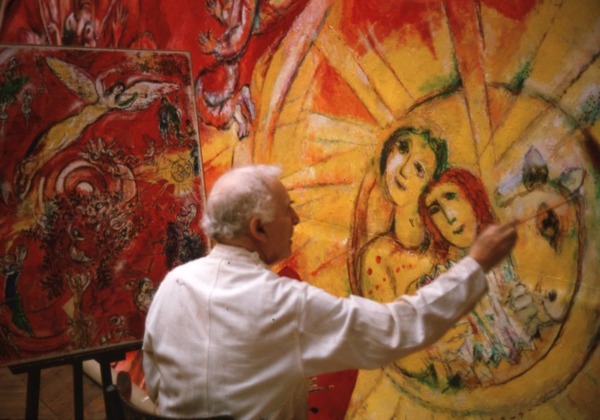 Artist painting a colorful mural with figures and vivid red and yellow hues, focusing on an angelic and celestial scene.