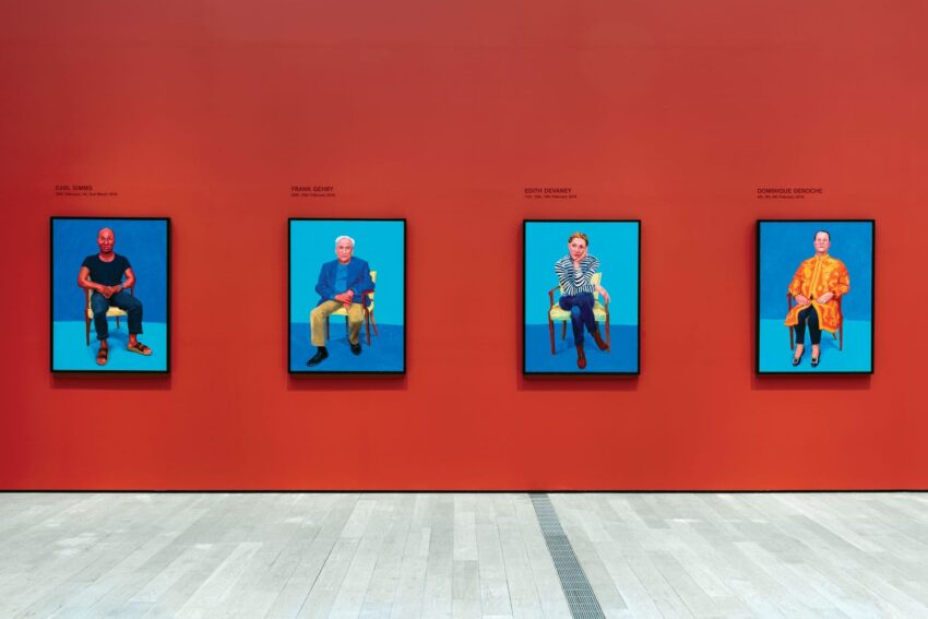Art gallery wall with four colorful portraits of seated individuals in front of a vibrant red background.