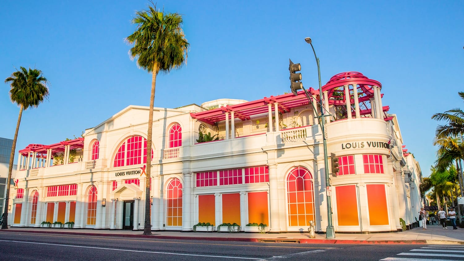 Colorful Louis Vuitton store exterior with red accents and palm trees under a clear blue sky in an urban setting.