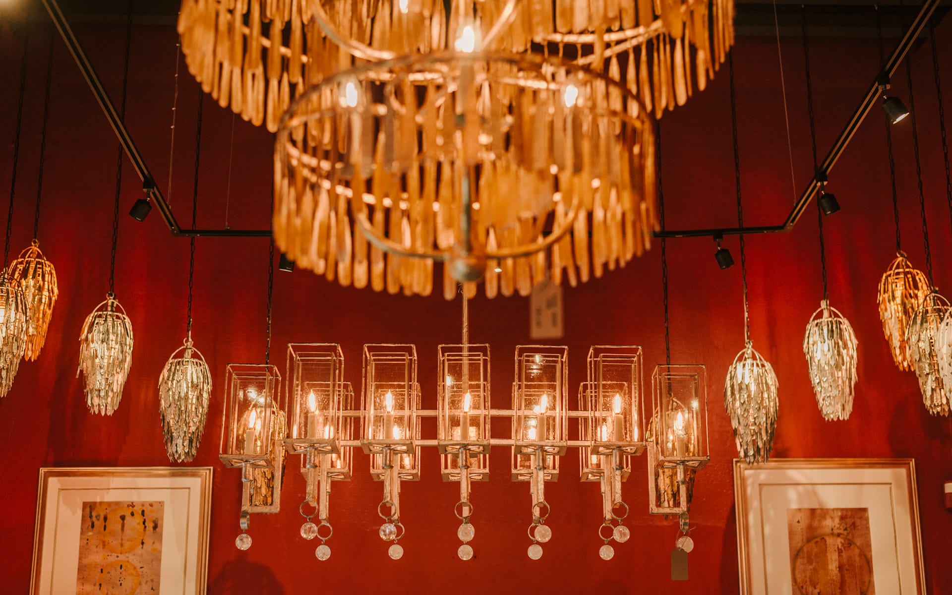 Warmly lit room with elegant hanging chandeliers and framed artwork on a red wall.