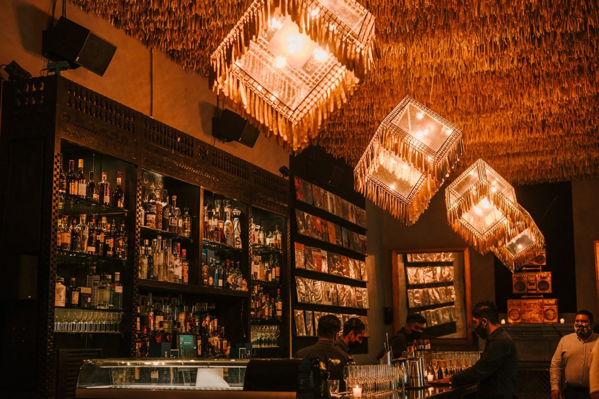 Cozy bar interior with unique ceiling lights, bottles on shelves, and bartenders serving patrons.
