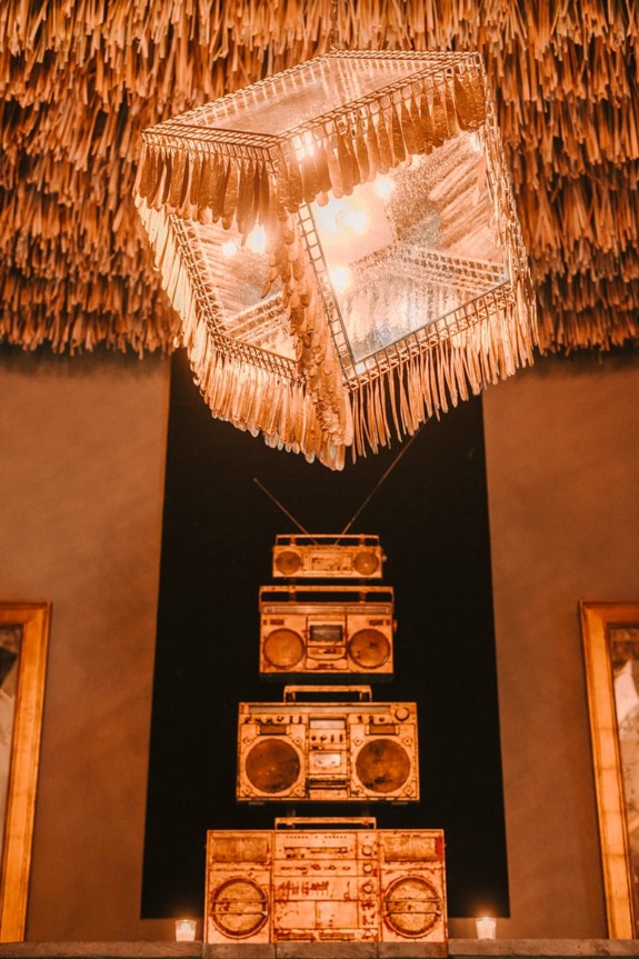 Unique chandelier resembling a cube with reflective surfaces, suspended above stacked vintage radios in a chic interior setting.