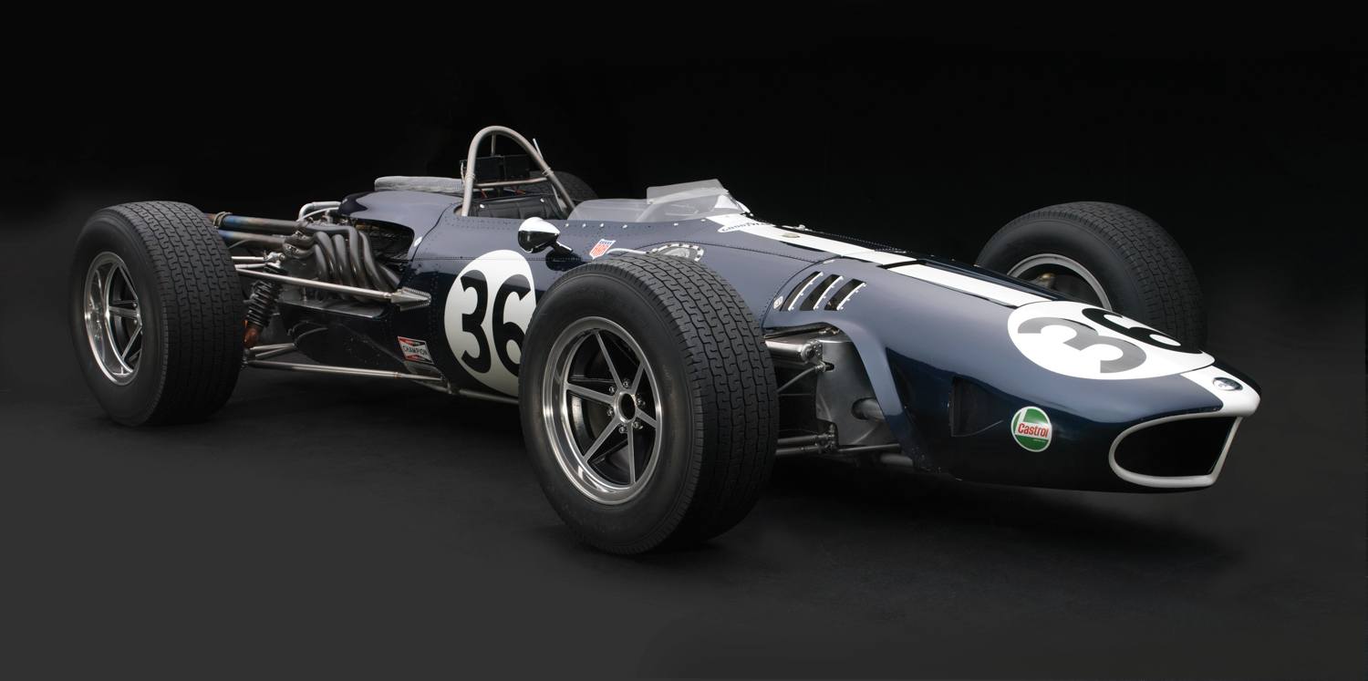 Vintage racing car with number 36, sleek dark body, exposed engine, and large tires against a black background.