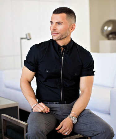 Man in black shirt and gray pants sitting on a chair in a modern room.