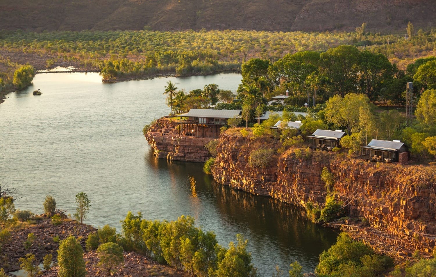 Scenic view of a river surrounded by rocky cliffs and lush green trees under a clear sky in a remote landscape.
