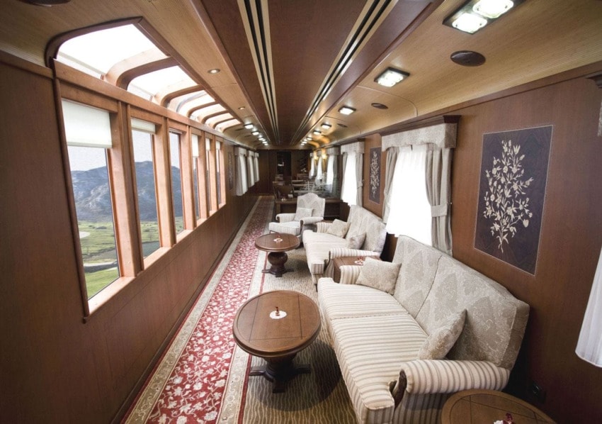 Luxurious train interior with plush sofas, wooden panels, and large windows overlooking scenic landscapes.