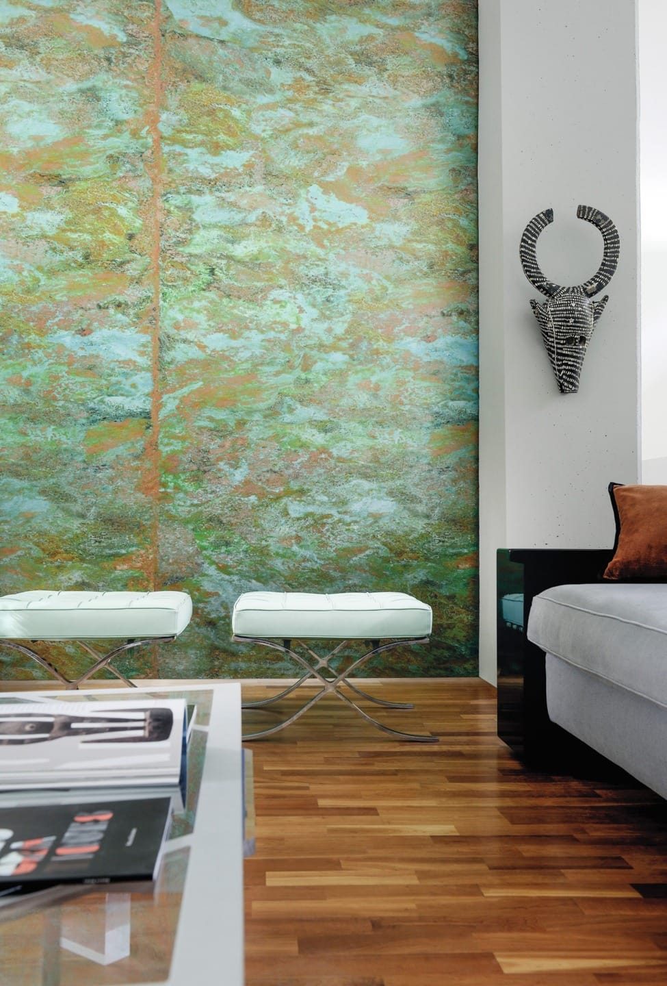 Modern living room with abstract green wall art, white benches, woven wall decor, wooden floor, sofa, and glass coffee table.