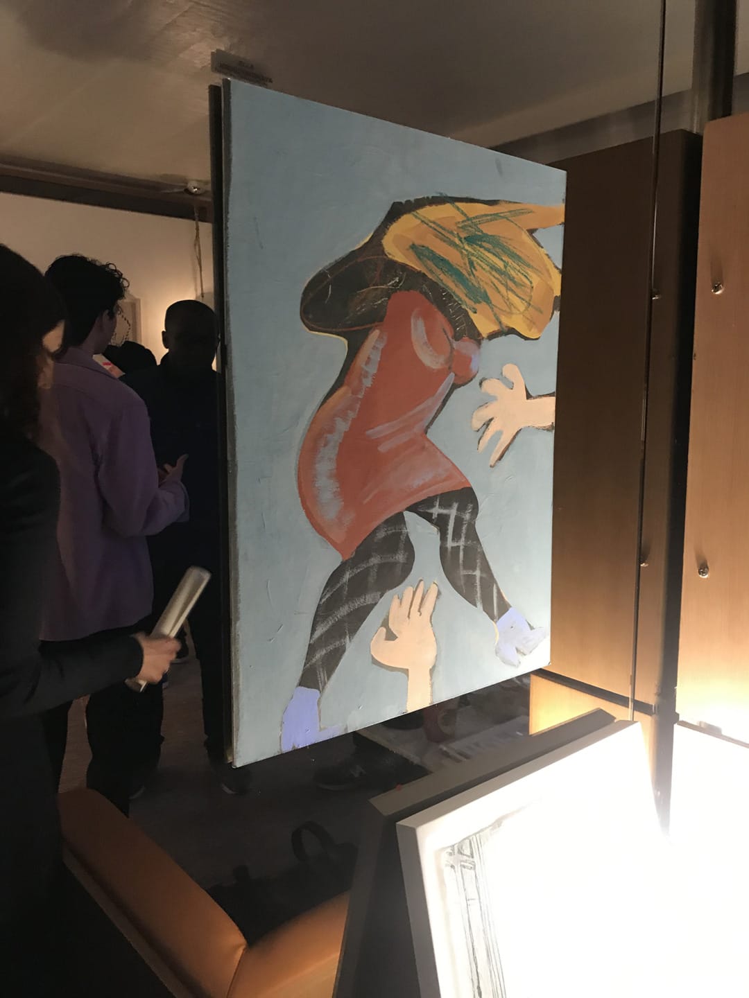 Abstract painting with vibrant colors and dynamic shapes on display in a dimly lit room with people observing.