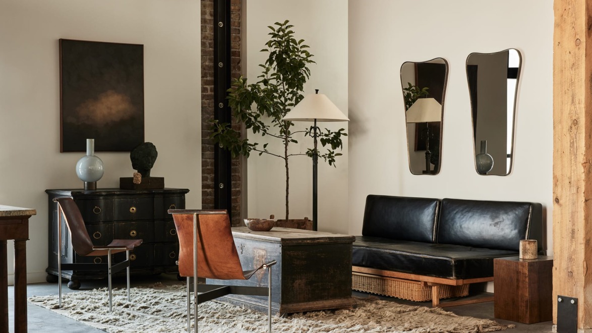 Stylish modern living room with leather couch, chic chairs, large rug, abstract art, lamps, mirrors, and indoor plant.