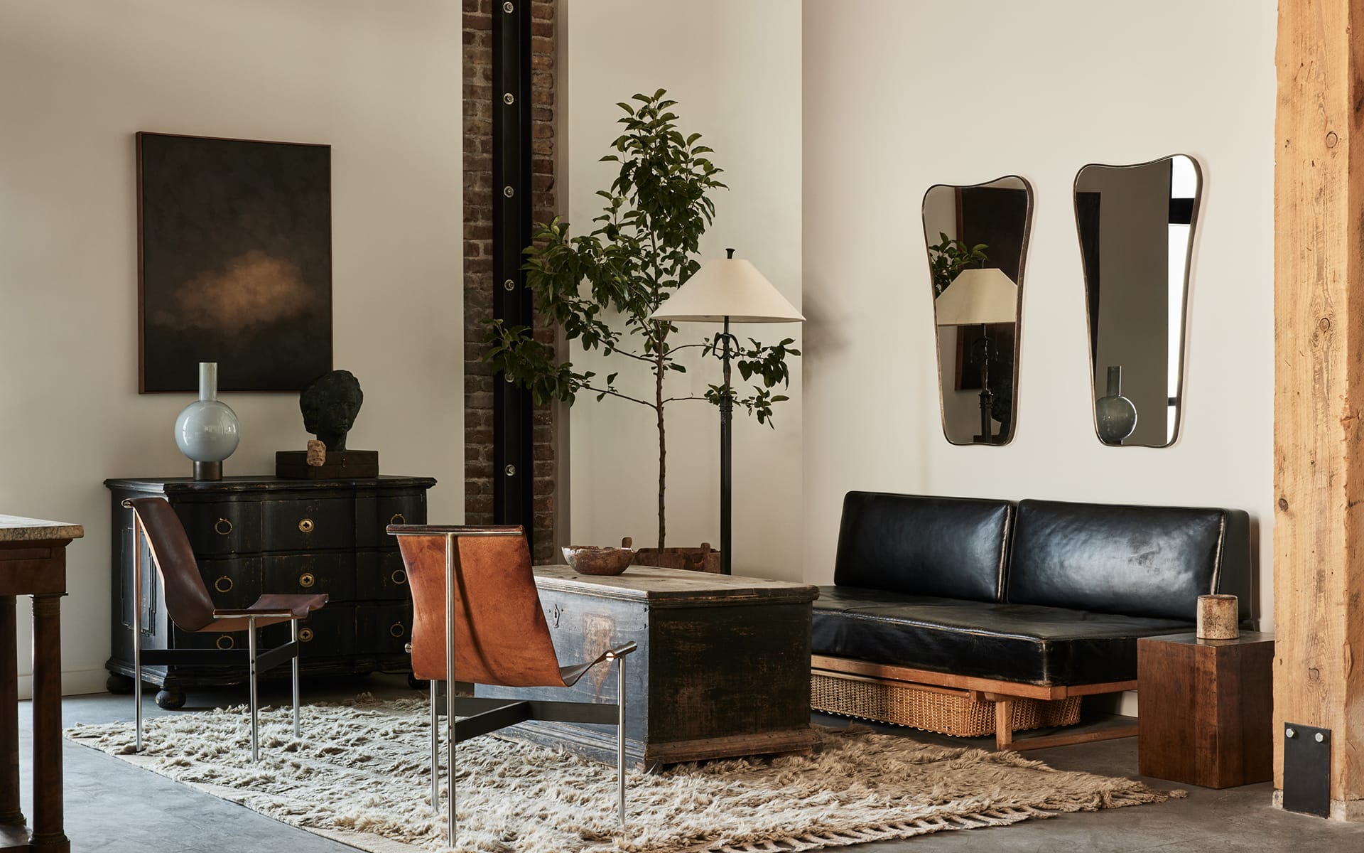 Stylish modern living room with leather couch, chic chairs, large rug, abstract art, lamps, mirrors, and indoor plant.