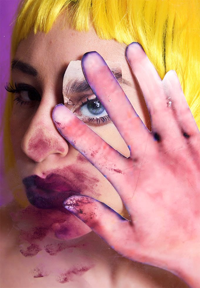Person with vibrant yellow hair presses hand against glass, displaying distorted fingers and intense eye contact.