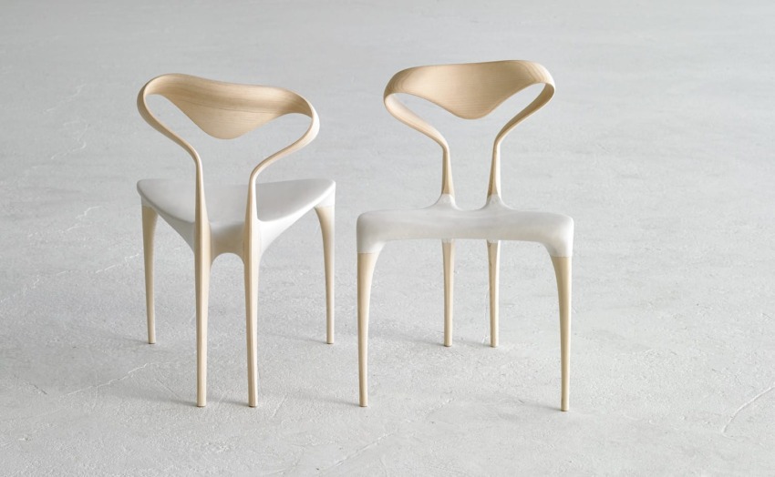 Two modern wooden chairs with unique curved backrests on a smooth, light gray floor.