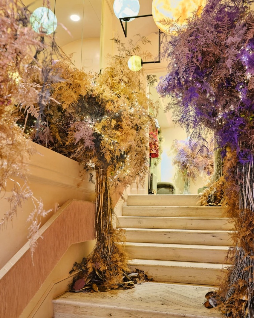 Staircase decorated with vibrant purple and gold flowers, illuminated by soft ambient lighting and hanging spherical lights.