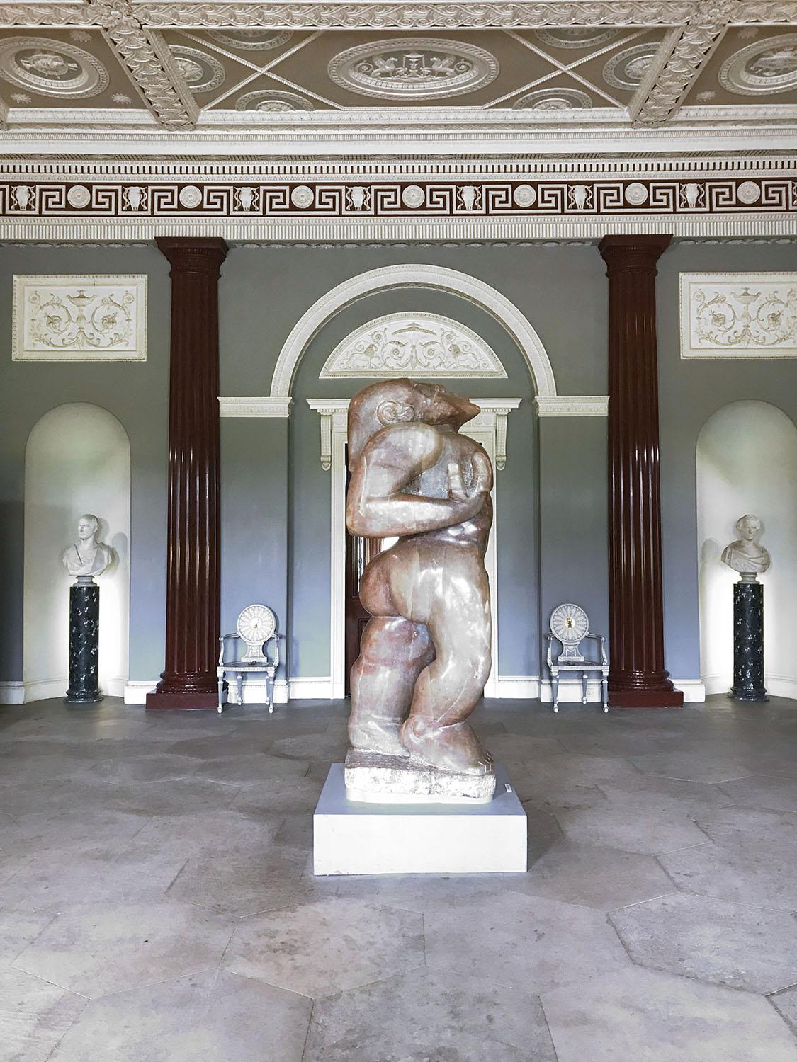 Marble statue of embracing figures in ornate gallery with busts and decorative ceiling.