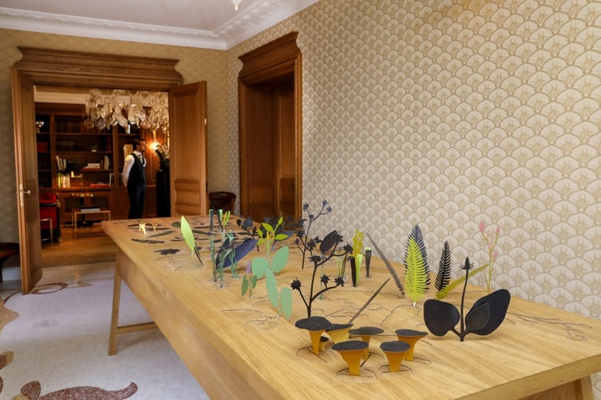 modern art sculpture display on wooden table in elegant room with classic wallpaper and open doorway to another room