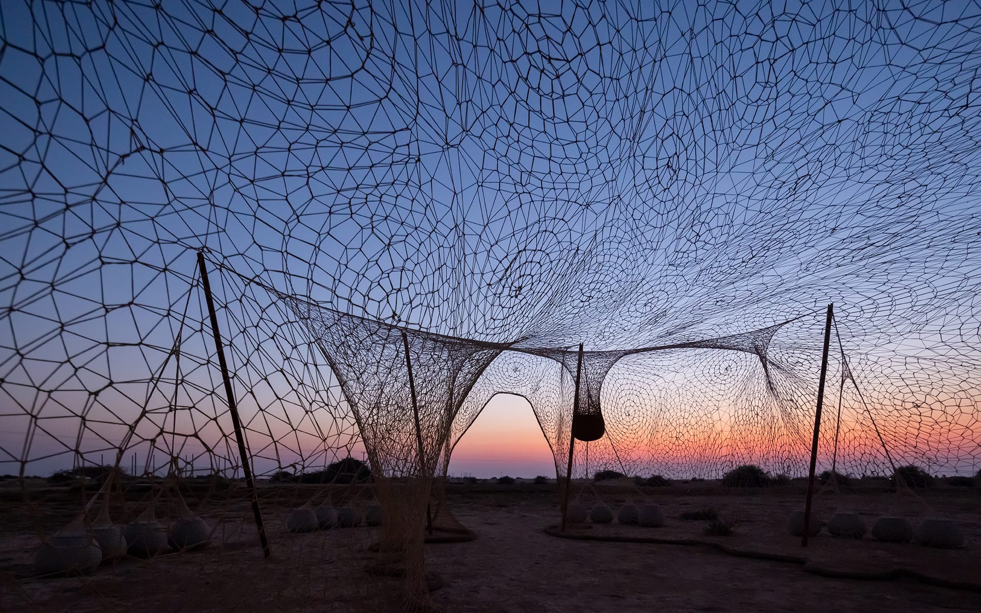 Artistic net structure at sunset with intricate patterns against a colorful sky, creating a captivating outdoor installation.