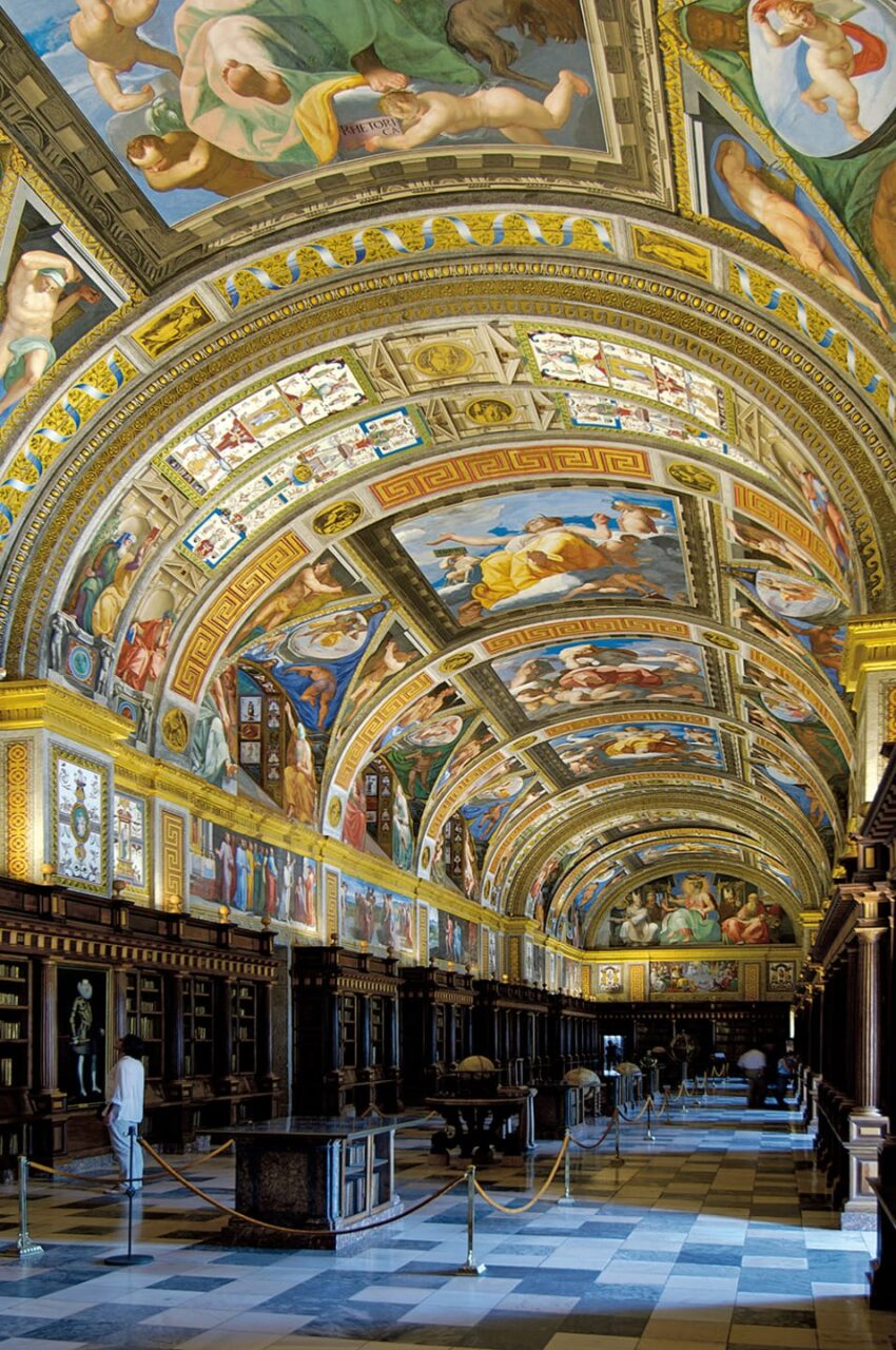 Ornate library hall with opulent painted ceiling and decorative arches, showcasing classical art and architecture.