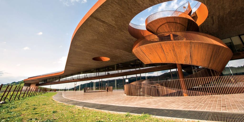 Modern architectural building with curved wooden design, featuring an open spiral staircase and large glass windows.