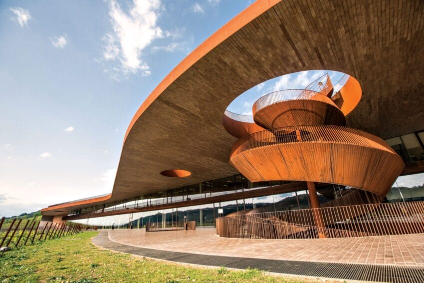 Modern architectural building with circular design elements and wooden accents against a blue sky backdrop.